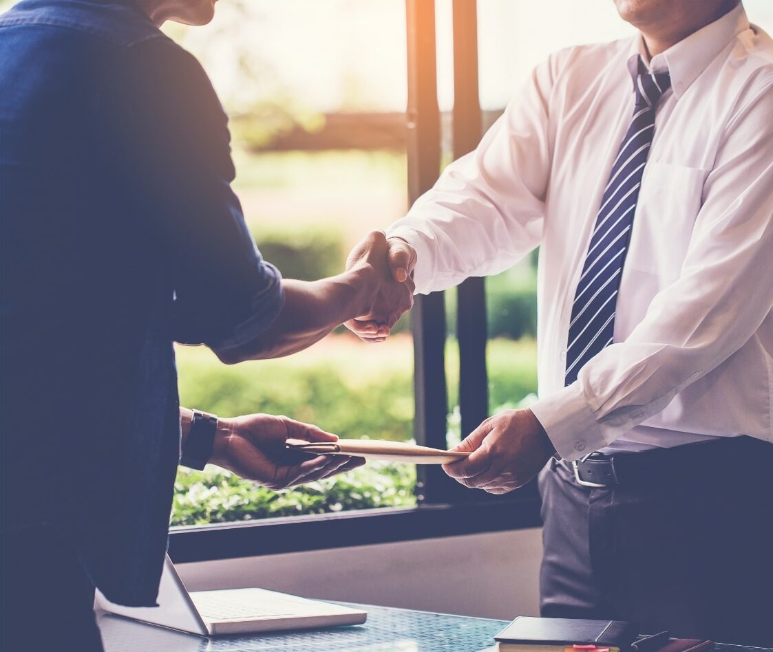 two men shaking hands over a site selection phase agreement.