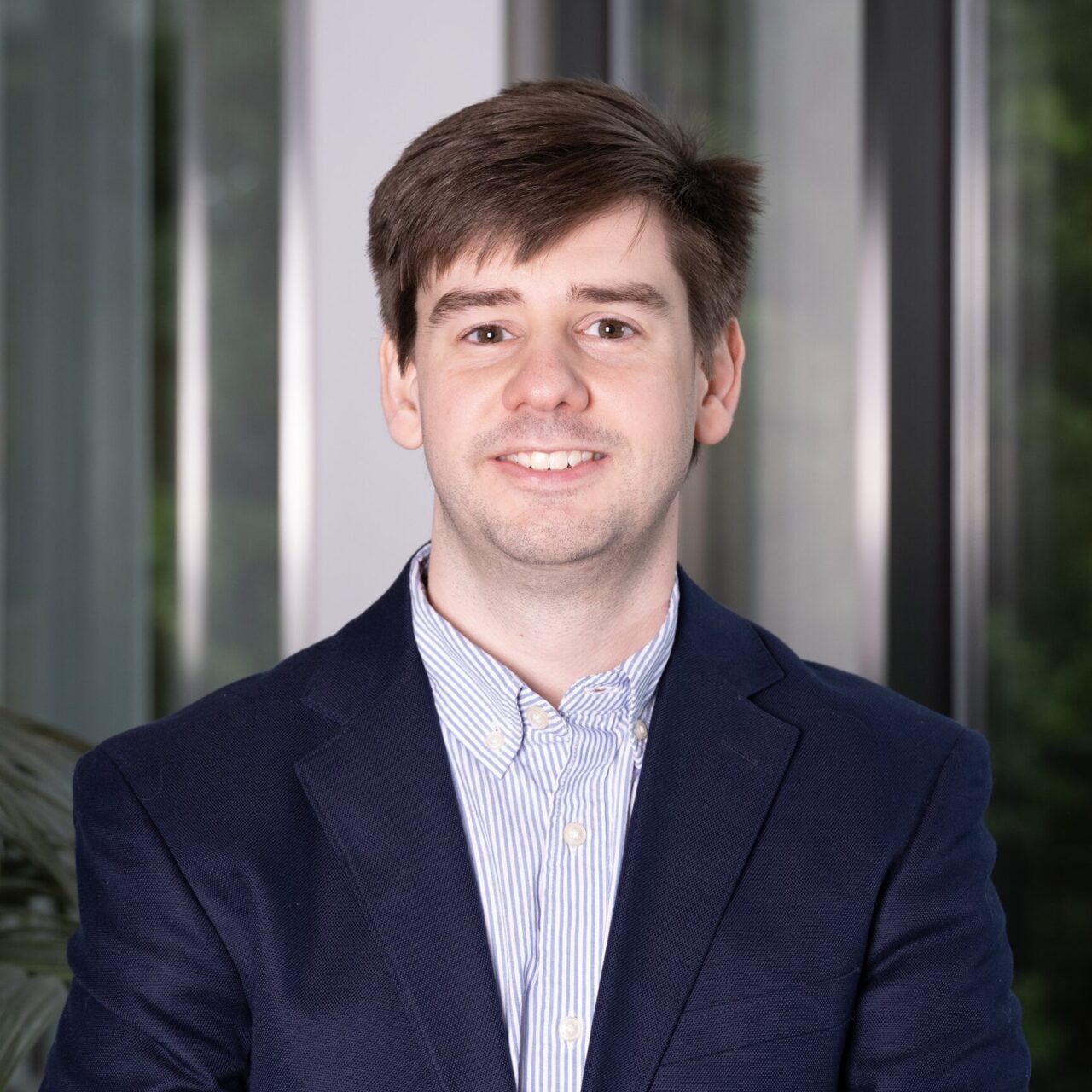 Man wearing a navy formal coat and button down shirt posing for a headshot
